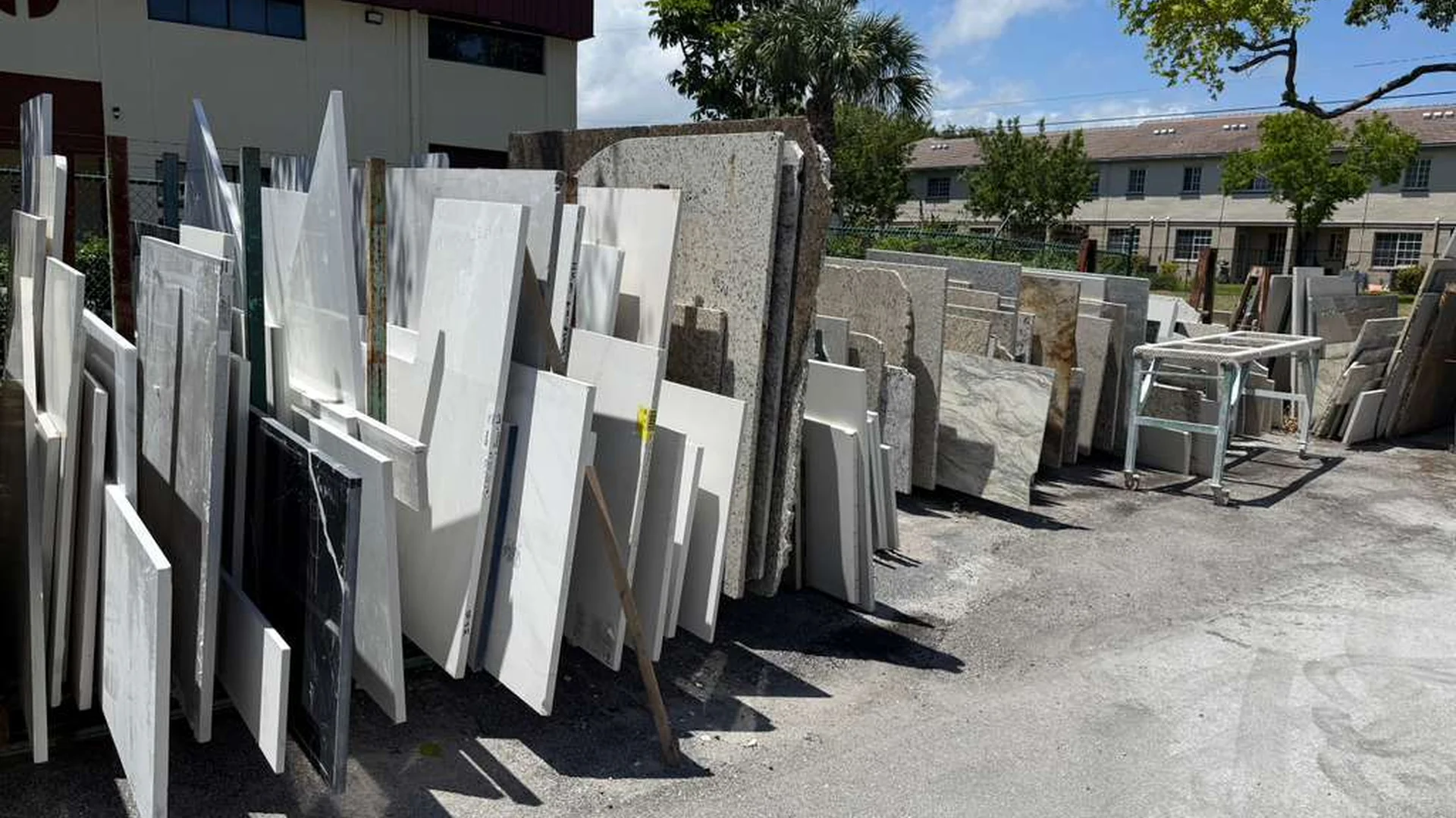Partial marble, quartzite, and quartz remnant slabs standing against tall wooden A-frame racks at the JR Stone Design yard in Riviera Beach, Florida