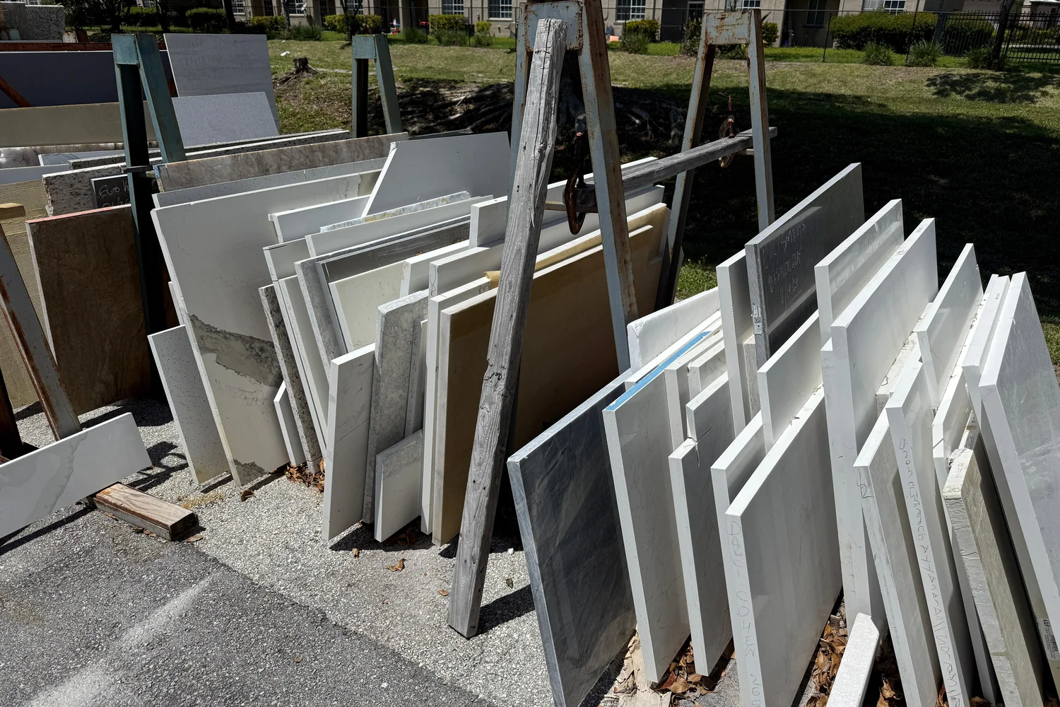 Wide view of the JR Stone Design outdoor remnant yard in Riviera Beach with rows of partial marble, quartzite, granite, and quartz slabs under blue sky
